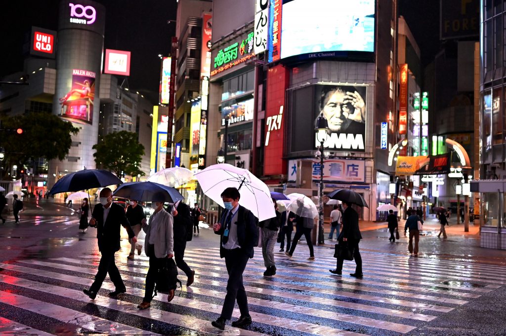 コロナウイルス感染を懸念してマスクを着用し、傘で雨から身を守りながら東京の横断歩道を渡る人びと（AFP）