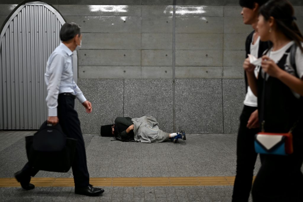 2020年6月18日、東京の有楽町駅にて人々が通り過ぎるなか歩道で寝る男性。（AFP）