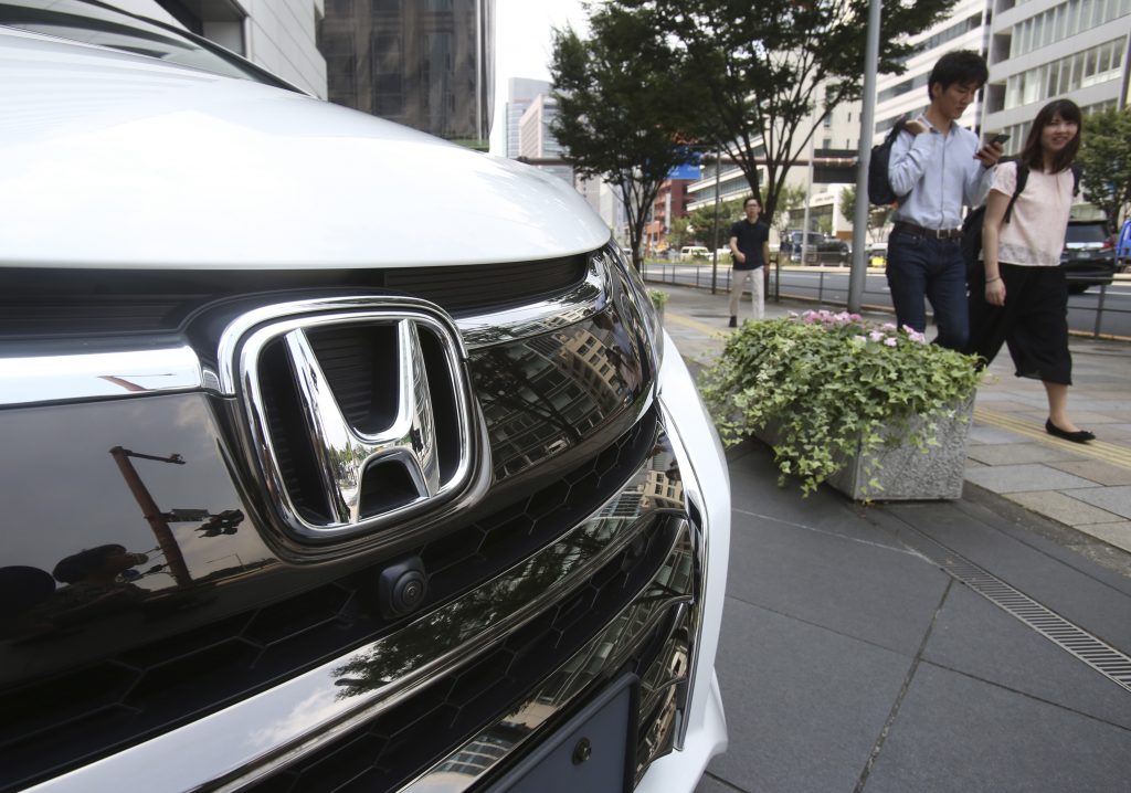 2019年7月31日、ファイル画像、東京の本田技研工業本社で展示されたホンダ車両前を通り過ぎる人々。日本の自動車メーカーであるホンダは2020年8月5日水曜、4〜6月期が赤字に落ち込んだことを報告した。特に、米国、日本、インドでの売上が新型コロナウィルスの感染拡大によって影響を受けた。(AP)