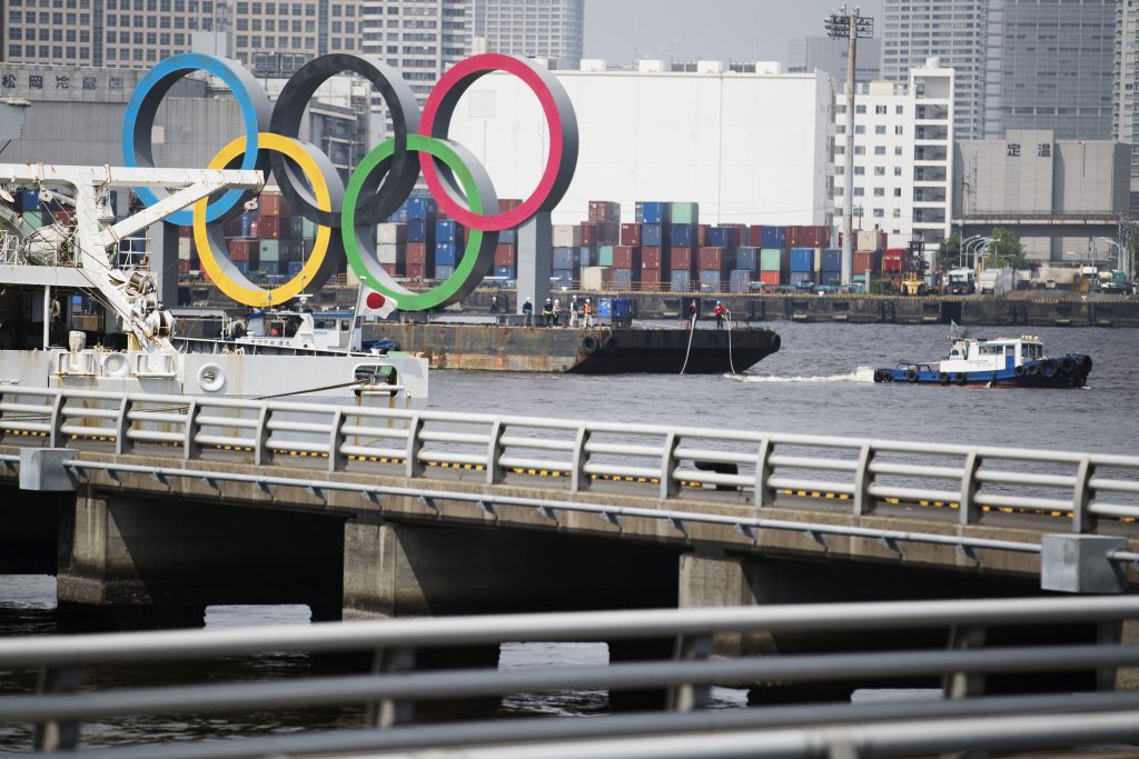 2020年8月6日(木)、東京・お台場海浜公園沖の通常の係留場所からえい航されるオリンピック・パラリンピック東京2020のための五輪シンボル。台船に載って東京湾に浮かぶ五輪シンボルは、木曜日にメンテナンスと称して撤去されたが、来年の大会を迎えるために再設置されると言う。東京オリンピックはコロナウイルス大流行により1年間延期され、2021年7月23日に開幕する予定。その後8月24日にパラリンピックが続く。(AP)