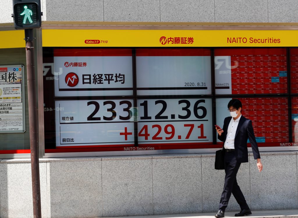 2020年8月31日に日本・東京の証券会社前の日経平均株価指数の画面の前を通り過ぎる男性。新型コロナウイルス感染症(COVID-19)のアウトブレイクを受けて防護マスクを着用している。(資料写真/ロイター)