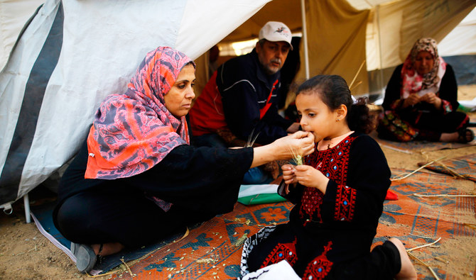 2018年4月3日、ガザ市の東部、イスラエルとの国境沿いで起きた抗議運動の後、パレスチナ人デモ隊とイスラエル軍の衝突現場付近にあるテントで娘に食べ物を与えるパレスチナ人女性。（AFP）