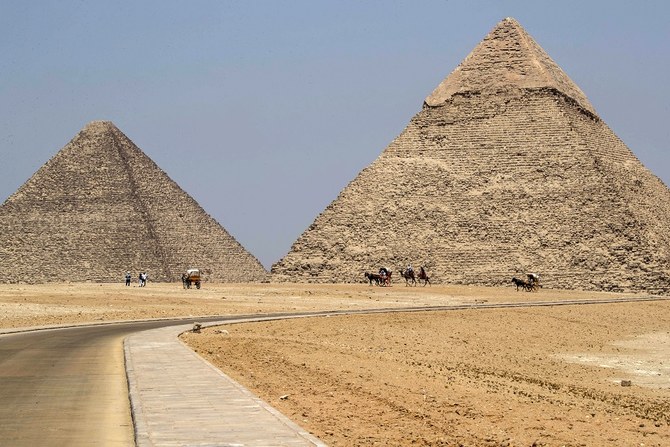 2020年7月1日に撮影されたこの写真には、エジプトの首都カイロの郊外南西部にある「ギザの墓地遺跡」に存在するクフ王の大ピラミッド（左）とカフラー王のピラミッド（右）付近で客待ちをするラクダを連れたガイドたちの姿が写っている。コロナ禍による行動制限が緩和され、遺跡観光も再開した。（資料写真/AFP）