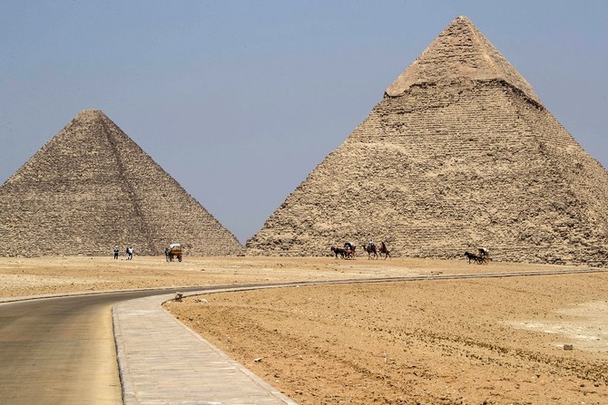 2020年7月1日に撮影されたこの写真には、エジプトの首都カイロの郊外南西部にある「ギザの墓地遺跡」に存在するクフ王の大ピラミッド(左)とカフラー王のピラミッド(右)付近で客待ちをするラクダを連れたガイドたちの姿が写っている。コロナ禍による行動制限が緩和され、遺跡観光も再開した。(資料写真/AFP)