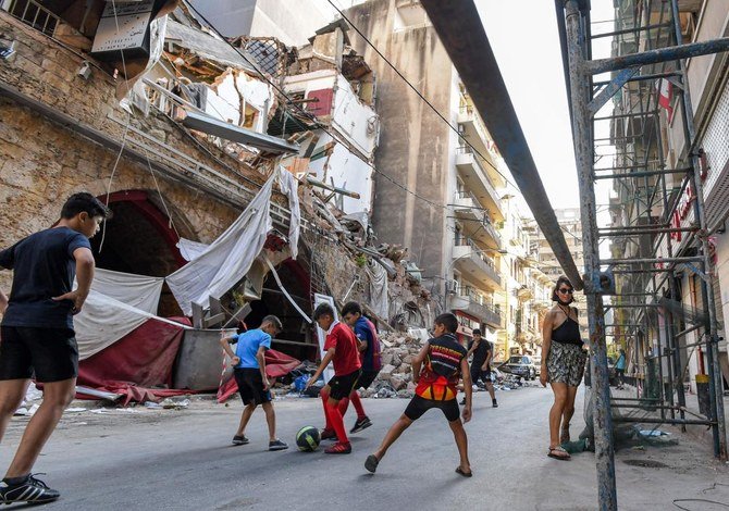 レバノンの首都ベイルート、ジュマイゼ地区。建物が崩壊し瓦礫が散乱する通りでサッカーをする子どもたちのそばを通る女性。2020年8月28日撮影。（AFP通信）