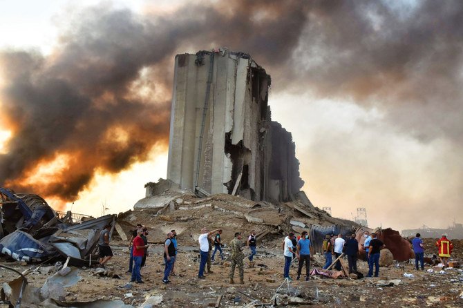 レバノンの首都を揺るがした2つの大爆発で煙が空に吹き上がり、数マイル先の建物を損傷させた後、消防隊員とショックを受けた見物人が瓦礫の下に閉じ込められた人々を捜索する（AFP）