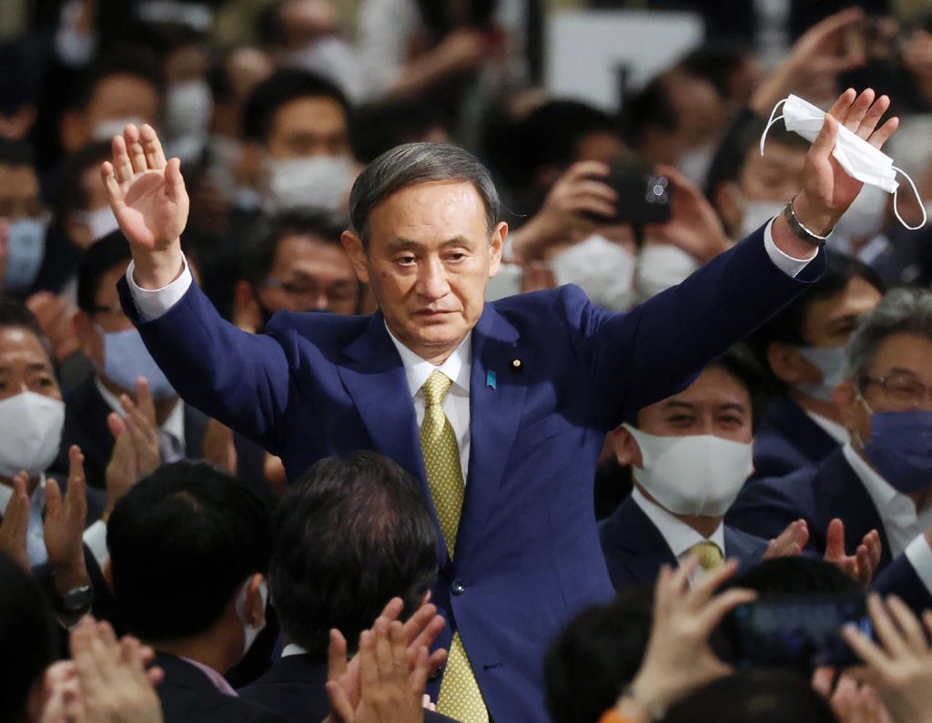 新総裁に選出され、議員たちの拍手に両手を上げて応える菅義偉官房長官。都内で行われた与党自民党の総裁選にて。2020年9月14日撮影。（AFP）
