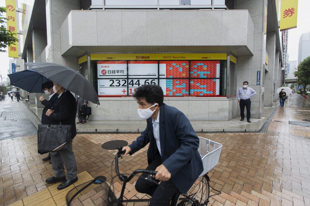 東京都内の証券会社前で、日本の日経平均株価指数を表示するスクリーンのそばに立って信号待ちをする人々=2020年9月25日 (提供写真 /AP)