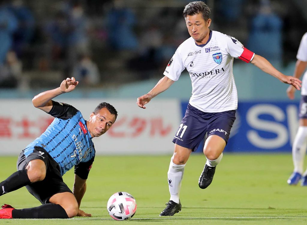 川崎フロンターレのFWレアンドロダミアン選手のタックルを受ける横浜FCのFW三浦知良選手（右）。2020年9月23日、川崎市の等々力競技場で行われたJリーグの横浜FC対川崎フロンターレ戦にて。