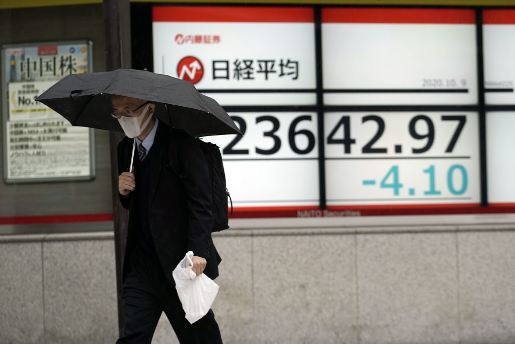 2020年10月9日（金）、雨の中、東京都内にある証券会社の日経平均株価を示す株価ボードの前を歩く男性。（資料写真/AP通信）