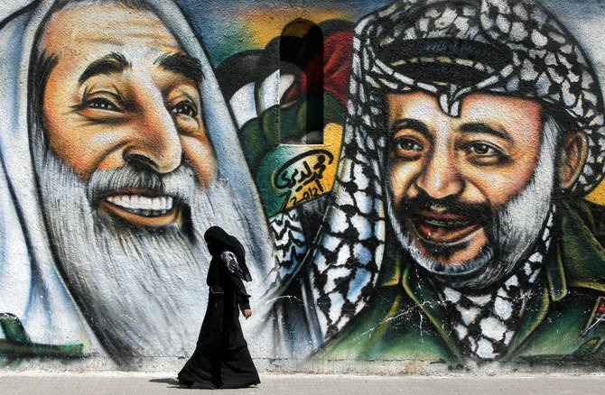 2012年7月4日、ガザ市で、ハマスの精神的指導者である故シェイク・アフマド・ヤシン氏（左）とパレスチナの指導者である故ヤセル・アラファト氏（右）を描いた壁画の前を歩くパレスチナ人女性。（写真：MAHMUD HAMS/AFP通信）