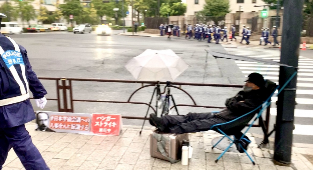 台風の到来を待ちながら、土砂降りの雨の中で椅子に座って、その抗議者はフランスの作家、エミール・ゾラの写真を見せた。（ANJ写真）