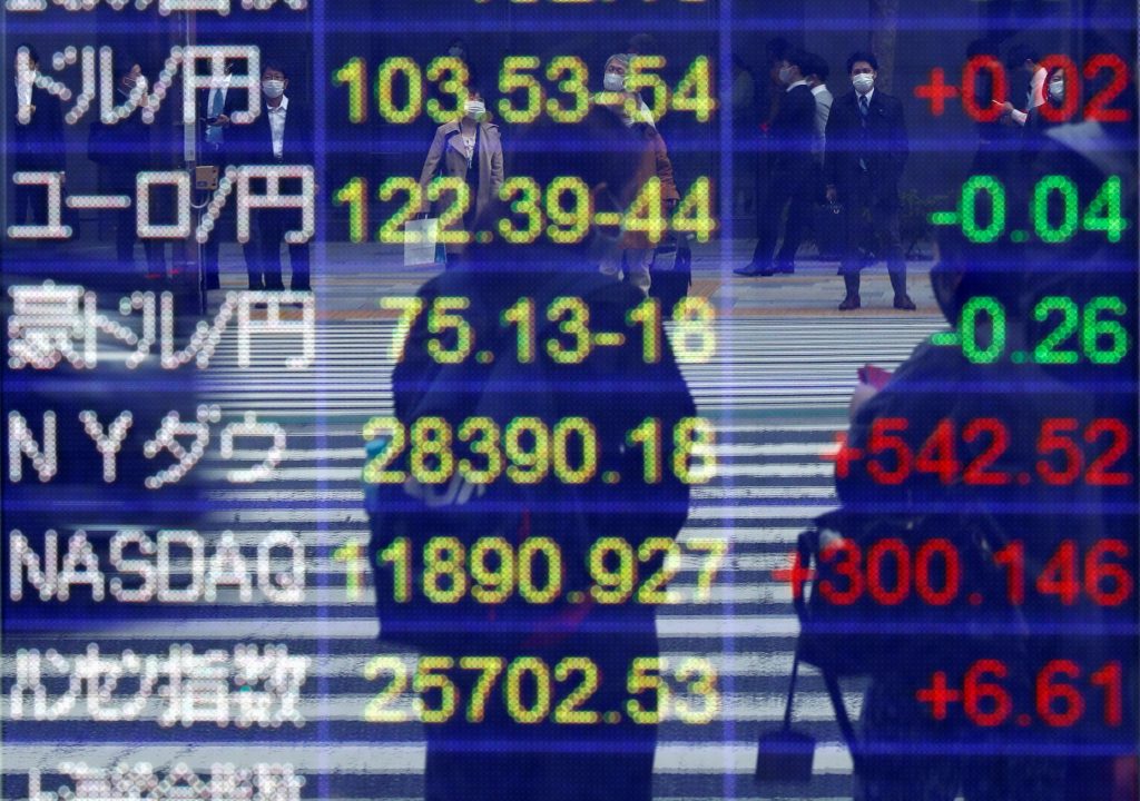 コロナウィルス感染症（COVID-19）が大流行する東京で、証券会社の外にある対ドル円相場やその他の通貨、世界の株価指数を表示する画面に映り込む、マスクを着用した通行人。2020年11月6日。（ロイター）