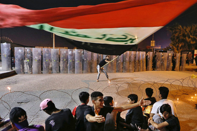 イラクのバスラで2020年11月4日、反政府デモが行われている場所を治安部隊が取り囲む中、デモ参加者らがイラクの国旗を振っている。（AP 写真／ナビル・アルジュラニ)