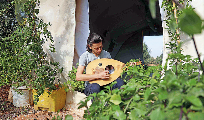 シリア北西部のイドリブ州アトマにて、幼少期の自宅を再現した青々とした草花に囲まれたテントでウードを演奏するウィッサム・ディアブ（19歳）さん。(AFP)