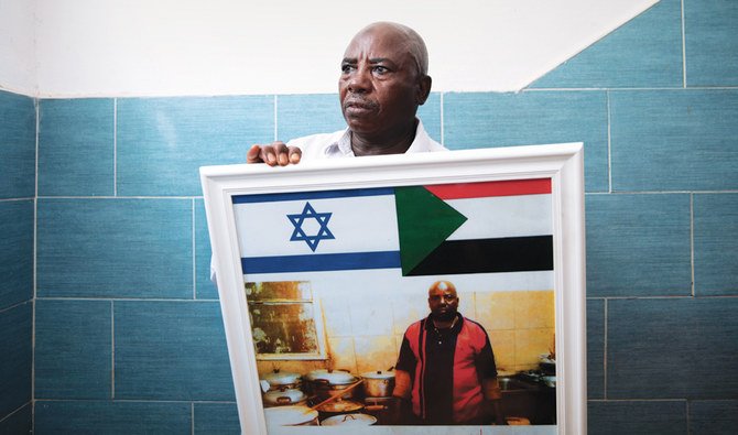 スーダンからの移民アトム・アリアルドムさん（56）。イスラエルのテルアビブ南部にある自宅の外で、スーダンとイスラエルの国旗で飾った自分の昔のレストランを写した写真を手にしている。（AP通信）
