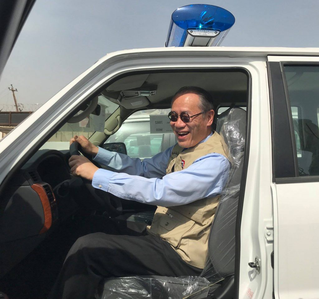 2018年3月21日に、駐イラク日本国大使館の公式Facebookページに公開された写真。イラク内の未特定の場所で、日本からイラク警察に提供された車の引き渡し式典の中で、岩井文男日本国大使がピックアップトラックに乗っている。（AFP）