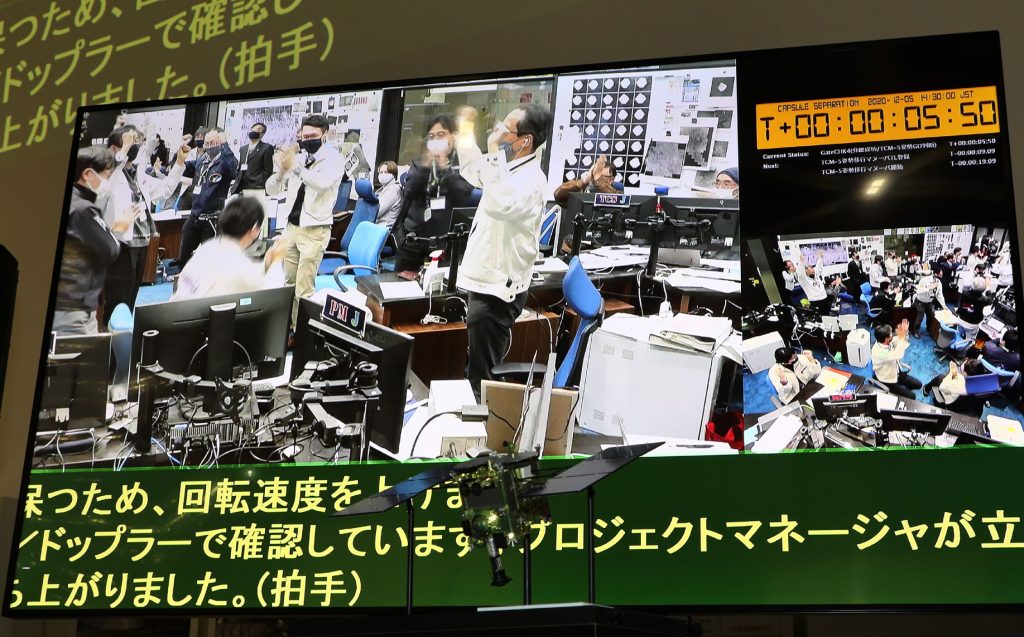 宇宙航空研究開発機構(JAXA)相模原キャンパス(神奈川県相模原市)で2020年12月5日、小惑星「りゅうぐ」から採取したサンプルが入ったカプセルを探査機「はやぶさ2」から分離することに成功した後、管制室で祝福する職員の姿がモニターに映し出された。(AFP / 時事通信)