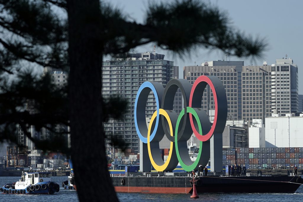 ファイル – 2020年12月1日のファイル写真に、オリンピックのシンボルが東京のお台場地区の平底荷船で運ばれる様子が写る。2020年度東京オリンピックの開催される年がやってくる。2021年がその年となる予定だ。9ヶ月前にオリンピックの延期が決まって以来、地元東京の運営団体とIOC は実施のタイミングを待ち続けている。彼らはパンデミックの渦中で、7月23日にオリンピックを再開する具体的方法については2021年の年明けまで待たなければならないと　語っていた。（AP写真）