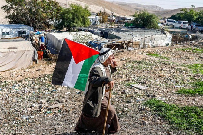 2020年11月29日、イスラエルに占領されたヨルダン川西岸地区のカーン・アル・アフマール村で、ベドウィンの男性がパレスチナの旗を持って歩く。(資料/AFP通信)