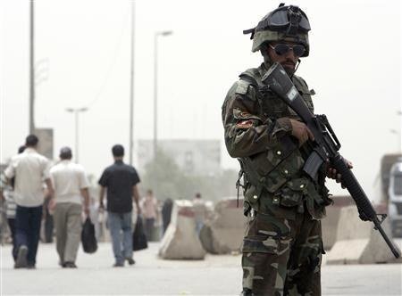 2008年5月18日、バグダッドのサドルシティの検問所に向かって歩く住民の近くで警備をするイラク兵士。（ロイター通信）