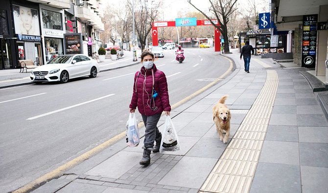 アンカラで27日、一人の女性が犬を連れて外出禁止令の最中に人気のない街路を歩く。トルコはCOVID-19を封じ込めるための予防措置を増強した。(AP)