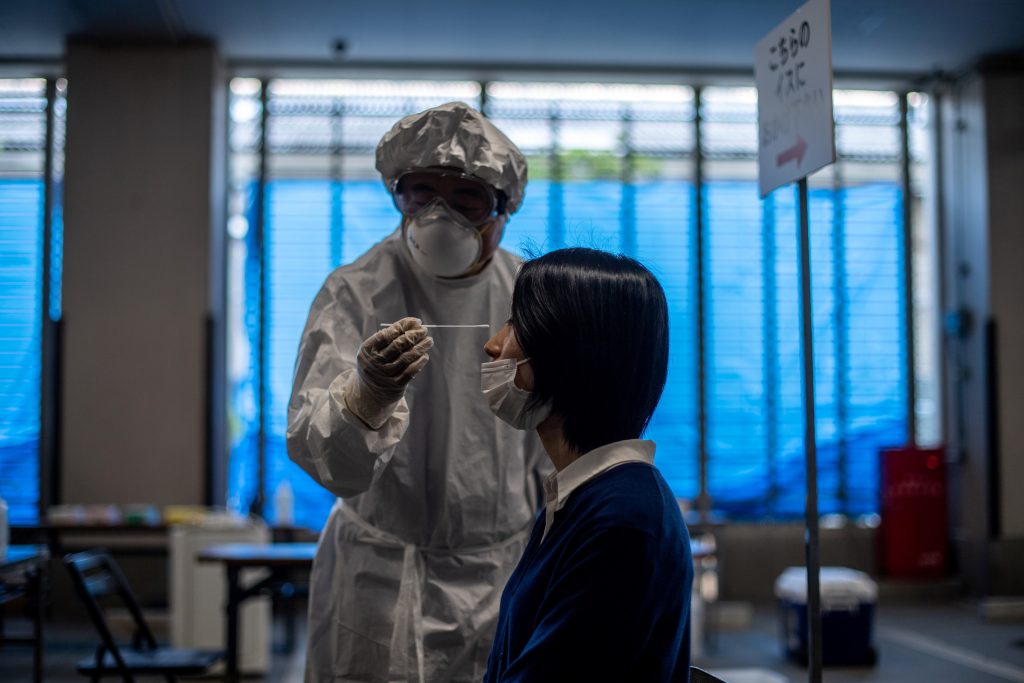 東京都品川のセンターで、防護服を着た医療スタッフ（左）と患者を務める職員が新型コロナウイルス感染症（COVID-19）のPCR検査のデモンストレーションを行う。 (AFP)