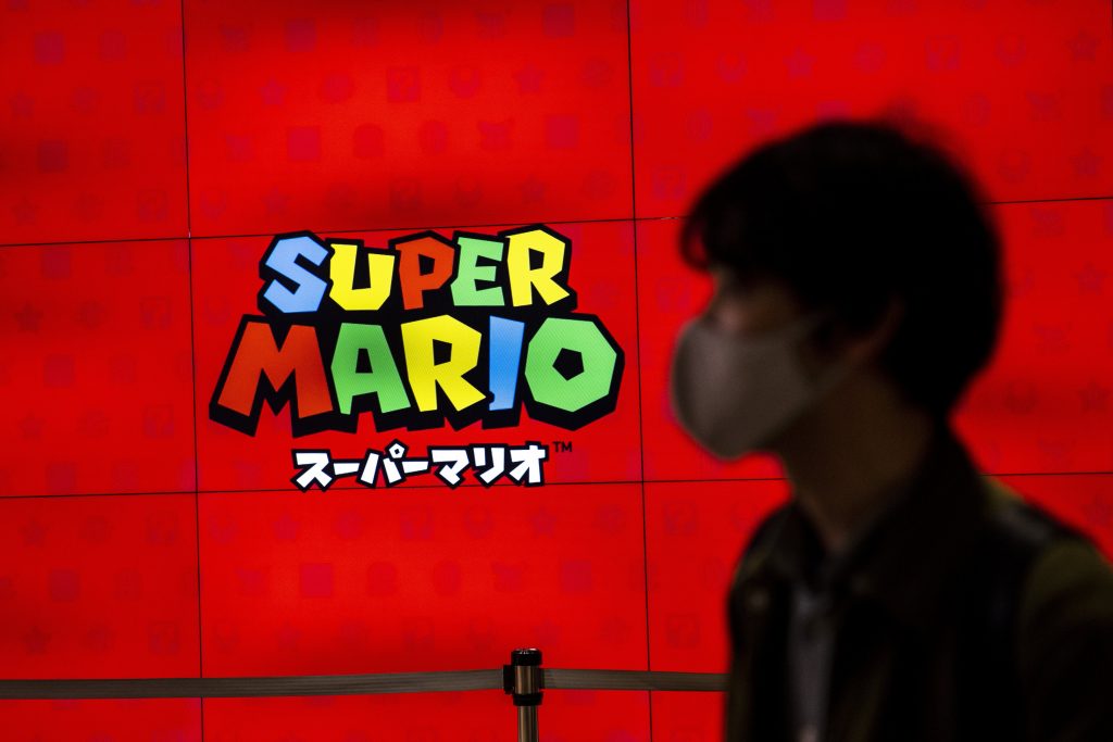 コンピューターゲーム、スーパーマリオのロゴの前を歩く男性。（2020年11月5日、東京都内にある任天堂の店舗で撮影）（AFP通信）
