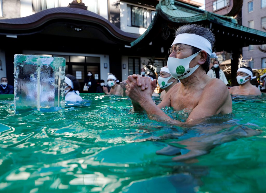 コロナウィルス伝染病（COVID-19）が蔓延する中、東京の鐵砲洲稲荷神社の儀式中に氷水の風呂に浸かって祈り、魂を清めパンデミックの克服を願う、保護マスクを着けた参加者たち。2021年1月10日撮影。ロイター/キム・ギョンフン