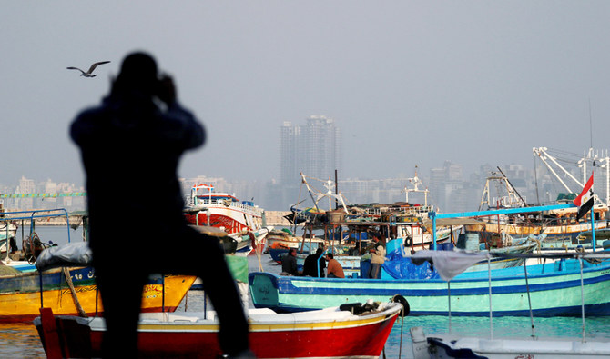 エジプト カイロ北部、地中海沿いに停泊する漁船の写真を撮る男性。2020 年 12 月 6 日。(ロイター)