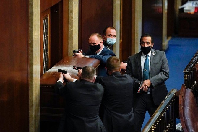 2021年1月6日水曜日、ワシントンの米国議会議事堂の下院本会議場に抗議者が侵入しようとする中、バリケードされたドアの近くで銃を持って立つ警察官。（AP通信の写真 / アンドリュー・ハーニク）