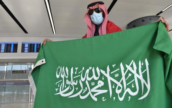 キングハーリド国際空港に親戚が到着するのを待つカタールとサウジの旗を掲げたサウジアラビアの男性。（AFP）
