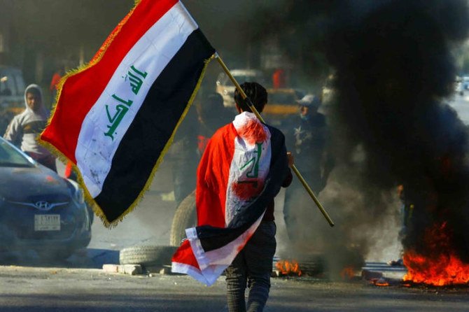 2020年1月12日、イラクのナジャフでの反政府抗議の最中に、燃えているタイヤの近くを歩きながらイラクの旗を掲げるデモ参加者。（ロイター）