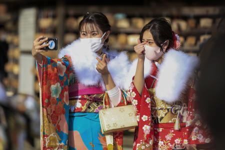 2021年1月11日月曜、東京都内で新型コロナウイルス感染防止のためマスクをつけ、成人（日本では伝統的に二十歳）となったことを祝うため、神社に参拝してセルフィーを撮影する着物姿の新成人女性たち。緊急事態宣言の発令下で、ほとんどの市区町村で式典が中止された。(AP)