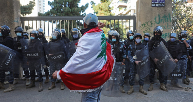 レバノン首都・ブリス通りのベイルート・アメリカン大学入口の外で行われたデモで、国旗に身を包んだ反対デモ参加者が警察に立ち向かう。（AFP）