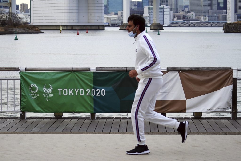 金曜日、お台場モニュメントの2020年東京オリンピック・パラリンピック大会バナー前を走る男性、 2021年1月8日、東京. (AP)