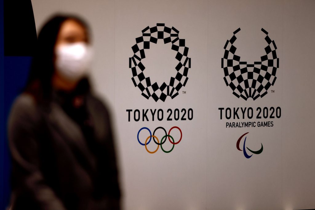 2021年2月2日、東京で、東京2020オリンピック・パラリンピック大会のロゴの前を歩いて通り過ぎるマスクをした女性。パラリンピックのアンドルー・パーソンズ会長は、観客を入れるかどうかに関わらず、パンデミックで延期された東京大会が今年開催され、「世界を変えるプラットフォーム」となることに自信を持っている。（AFP通信）