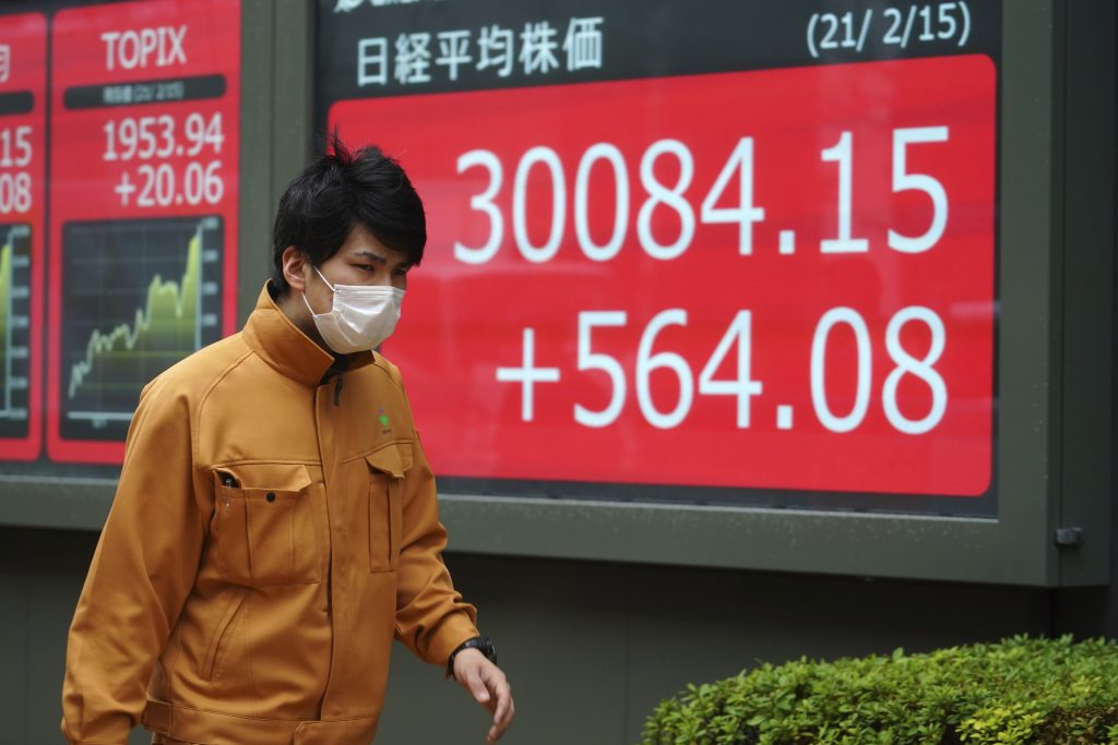 日本の日経225指数を示す証券会社の電子株価ボードの前を歩く、マスクを着用した男性。2021年2月15日、東京。（資料写真/AP）
