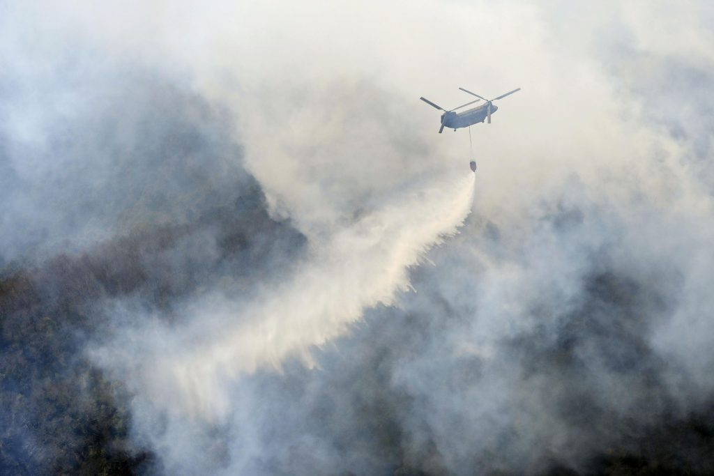 2021年2月24日(水)、東京の北、栃木県足利市で発生した山火事に、ヘリコプターが放水する様子を見る住民。(ファイル写真 / 共同通信 AP経由)