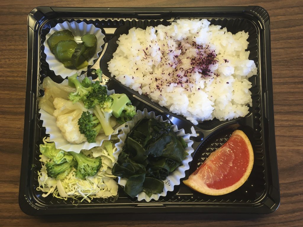 2021年2月4日、東京のホテルの一室での隔離中に出された朝食のベジタリアン弁当が映っている。1日3回、弁当が届けられる。 メニューは、野菜の煮込み、わかめの酢の物、新鮮な野菜のサラダ、グレープフルーツ1切れ、ご飯とふりかけ、付け合わせの漬物。（APの写真/オノ・マユコ）