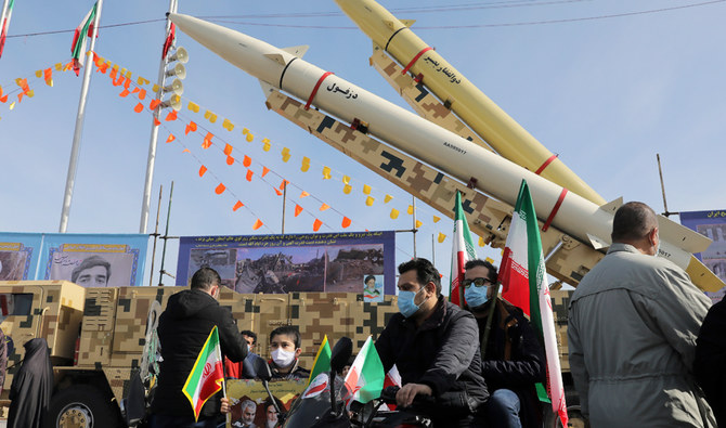 2021年2月10日、水曜日、イラン、テヘランのアーザーディー（自由）広場で、イスラム革命42周年を祝う集会の間に、イラン人たちがオートバイでミサイルの前を通過する。（AP通信）