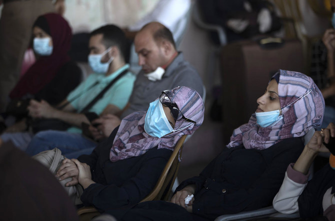 2020年9月27日撮影のこのファイル写真には、エジプトとの国境にあるガザ地区南部のラファ国境検問所で、マスクをつけたパレスチナ人たちが荷物の横に座り、越境を待つ様子が写されている。(AP写真/Khalil Hamra、ファイル写真)