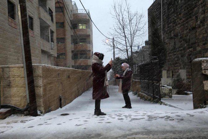 2021年2月17日、ヨルダン川西岸の都市ラマラで雪が降る中、パレスチナ人女性が写真を撮っている。（AFP）