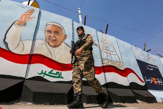 バグダッドのシリアカトリック聖母受胎教会の外にあるイラクの国旗の横で手を振るフランシスコ教皇を描いた壁画の前を歩くイラク軍兵士（AFP）