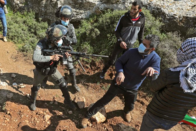 占領下の北ヨルダン川西岸のビトダジャン村で2021年3月5日、ユダヤ人入植地に反対するデモの最中にイスラエル軍兵士がパレスチナ人の抗議者に向けて銃を向ける（AFP通信）