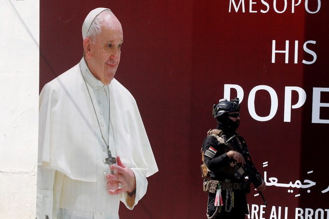 2021年3月3日、フランシスコ教皇の訪問に先立ち、イラクのバグダッドで警備員が教皇のポスターの隣にたたずむ。（ロイター）