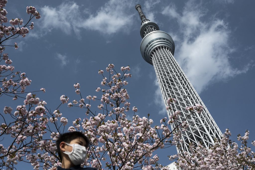 桜と高さ634メートルの日本一高い建造物「東京スカイツリー」の下で遊ぶ子ども = 2021年4月1日、東京（AFP通信）
