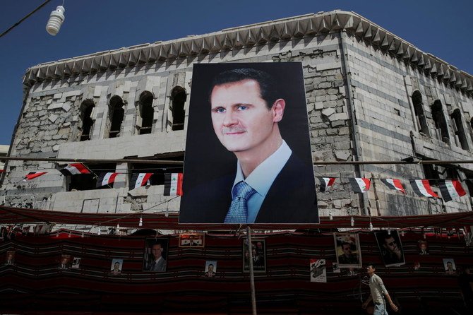 2018年9月17日、シリアのダマスカス郊外のドウマで、シリアのバシャール・アル=アサド大統領を描いた垂れ幕の脇を人が通り過ぎてゆく。（ロイター）