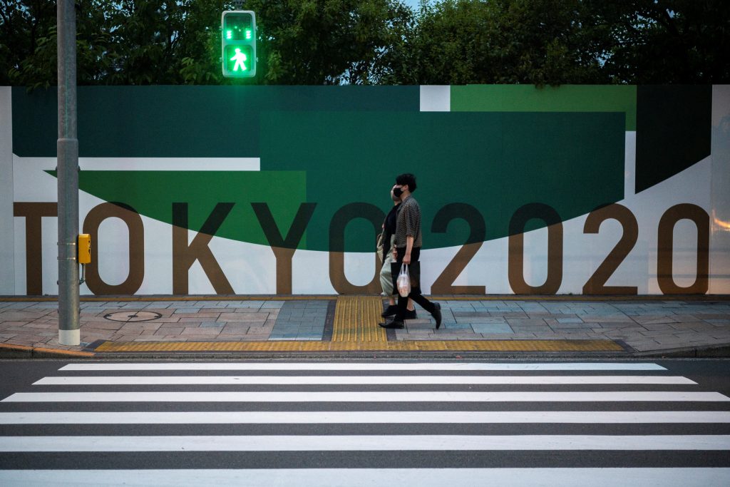 20201年5月10日、東京の街に貼られた2020年東京オリンピックのポスターの前を通り過ぎるカップル(AFP)