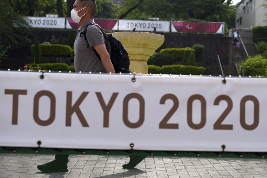 2021年5月25日、新型コロナ感染防止用のマスクを着用しながら、東京オリンピックを知らせる横断幕の横を歩く男性（AP Photo/ユージン星子）